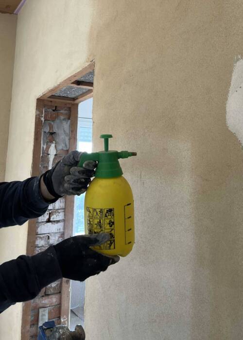 Artigiano che pre-umidifica un muro molto assorbente prima dell’applicazione dell’intonaco in argilla.