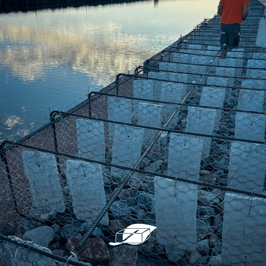 Struttura galleggiante in rete metallica con file di piastrelle bianche verticali fissate, immerse parzialmente in acqua calma; sullo sfondo si vede il cielo riflesso.