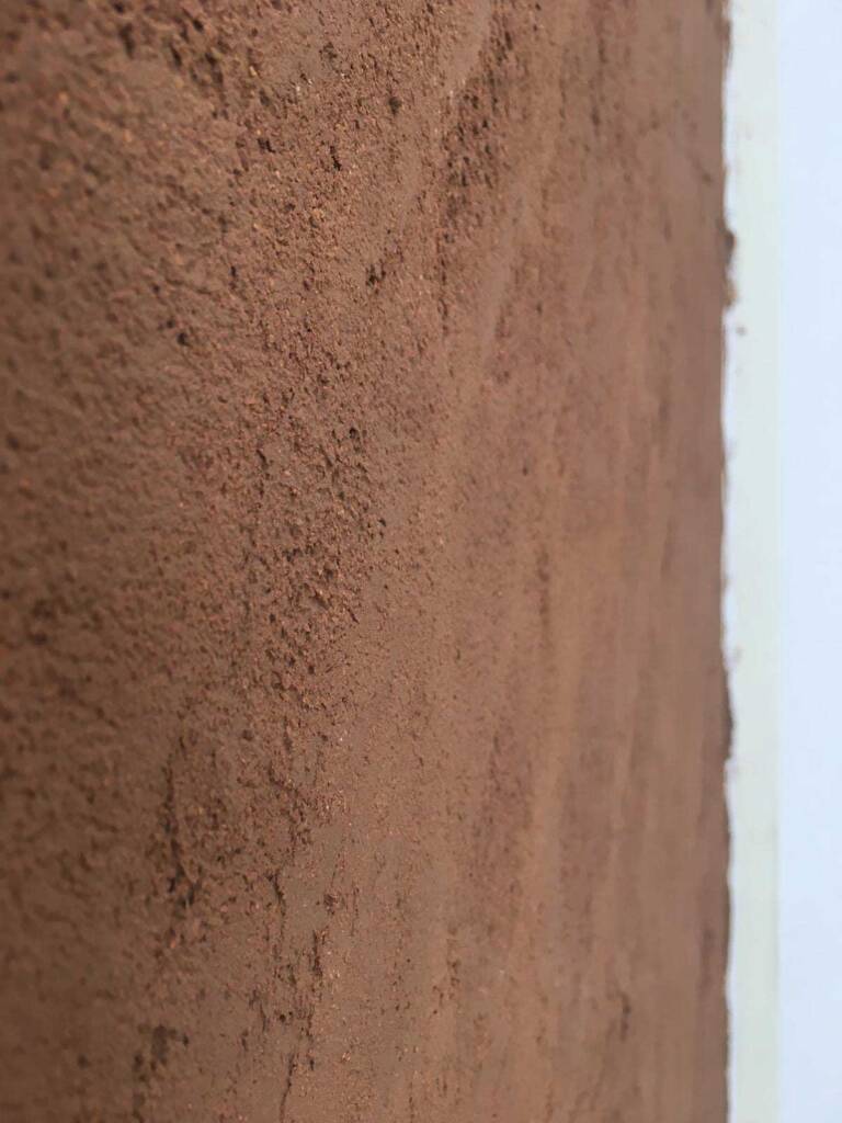 Primo piano di una parete con intonaco in argilla dal colore caldo e texture grezza. Soluzione naturale per ambienti salubri.