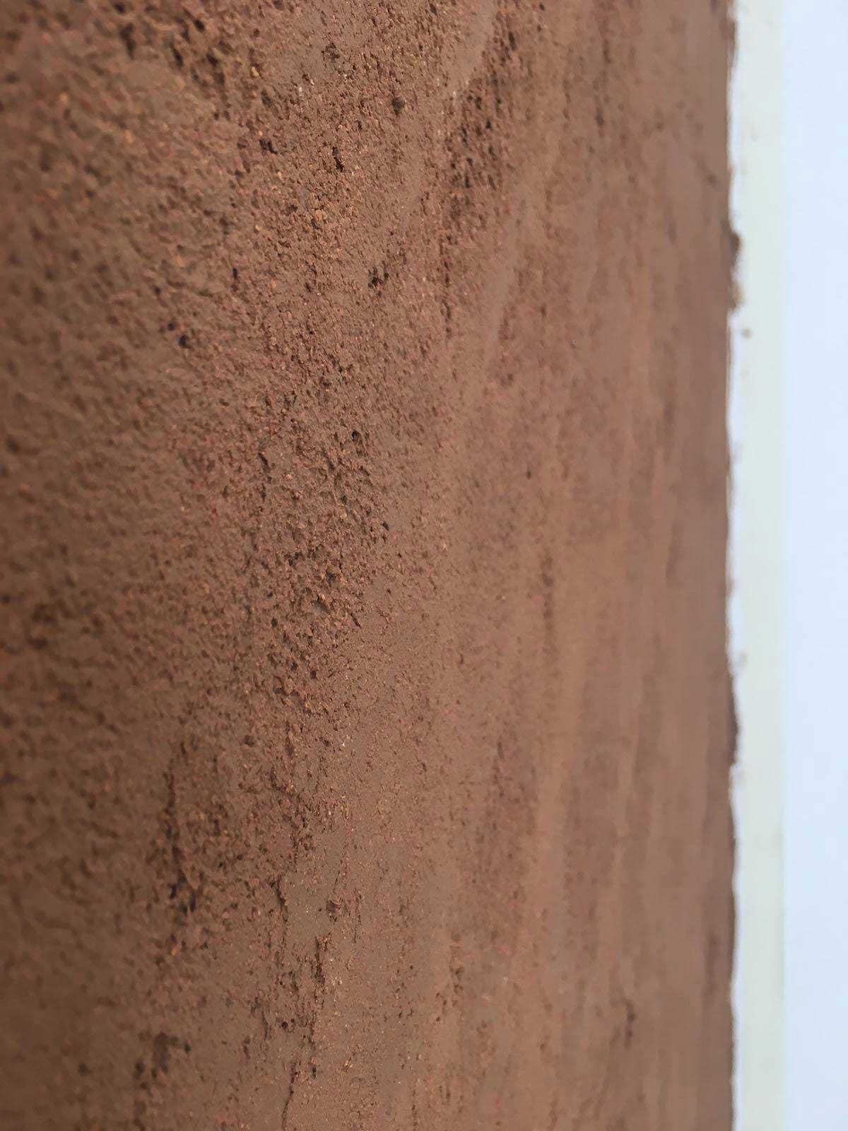 Dettaglio ravvicinato di una parete rifinita con intonaco in terra cruda, dalla texture materica e calda, tipica delle soluzioni Terragena.