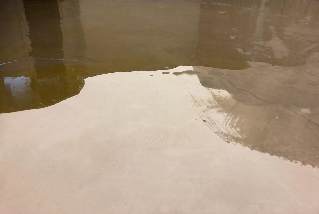 Dettaglio di un pavimento in terra cruda durante la fase di stesura dell'olio, con riflessi lucidi e superficie parzialmente opaca.