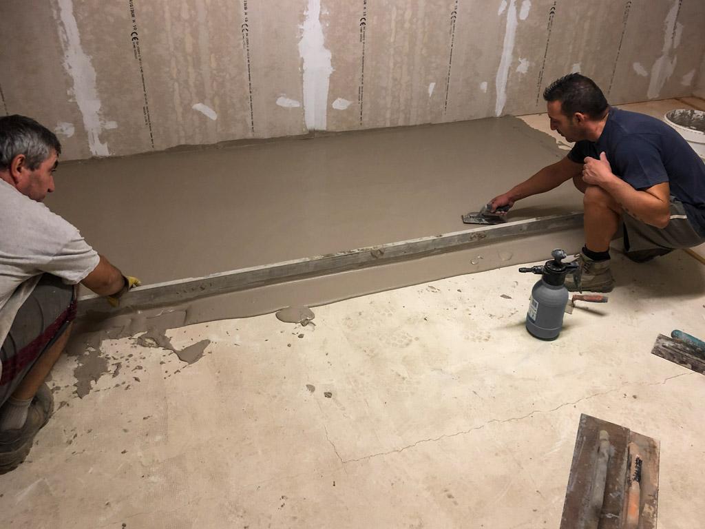 Due operai in ginocchio che stendono il pavimento in terra cruda.